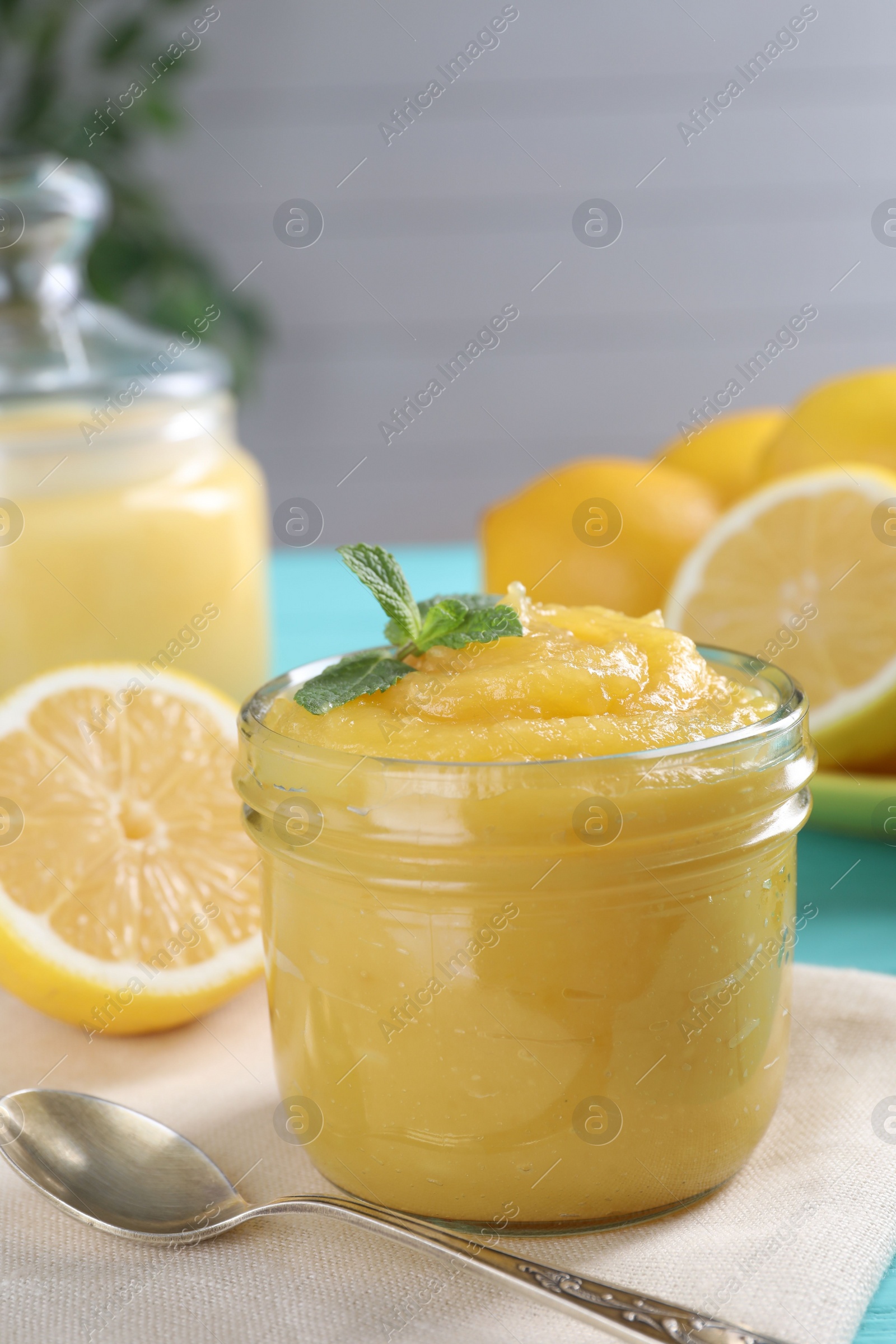 Photo of Delicious lemon curd in glass jar, fresh citrus fruits, mint and spoon on table