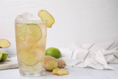 Photo of Glass of tasty ginger ale with ice cubes and ingredients on white tiled table, space for text