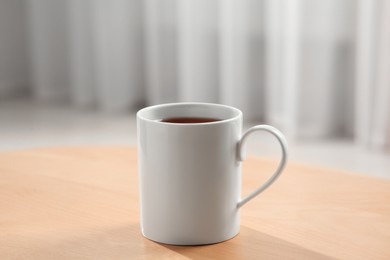 Photo of White mug with drink on wooden table indoors. Mockup for design