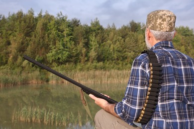 Photo of Man with hunting rifle near lake outdoors, back view