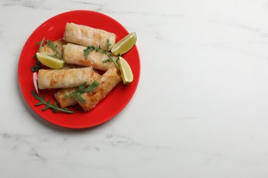 Photo of Plate with tasty fried spring rolls, arugula and lime on white marble table, top view. Space for text