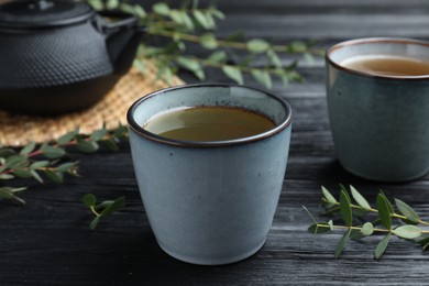 Photo of Cup of aromatic eucalyptus tea on black wooden table, closeup