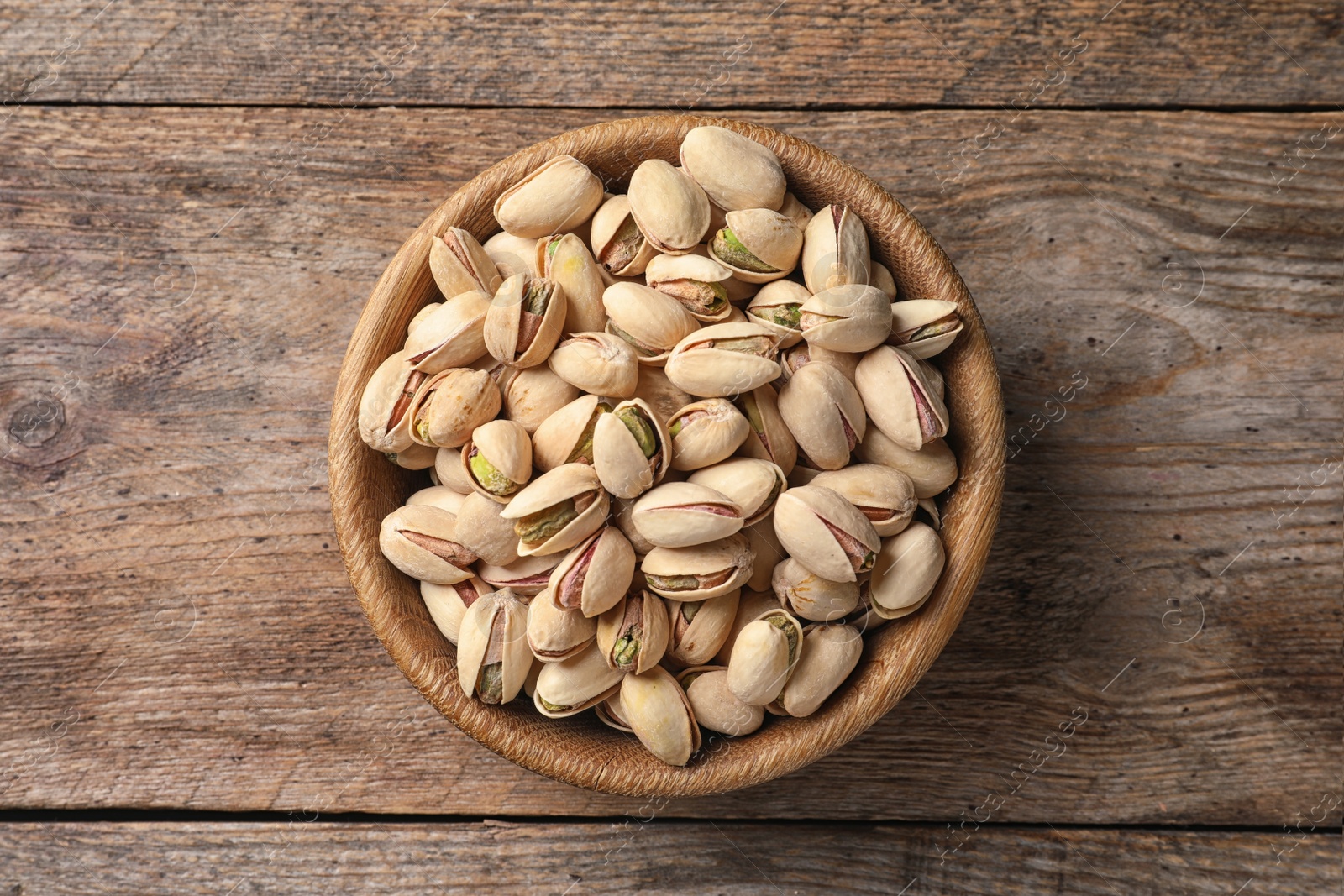 Photo of Organic pistachio nuts in bowl on wooden table, top view