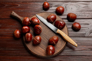 Photo of Roasted edible sweet chestnuts and knife on wooden table, flat lay