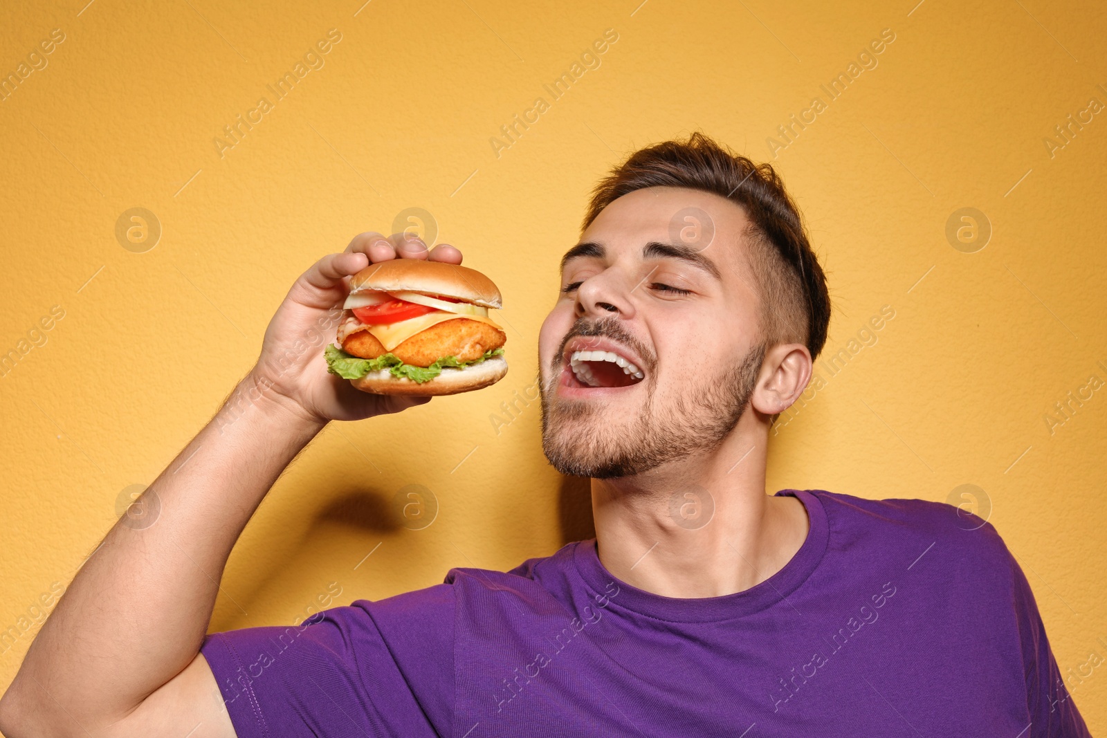 Photo of Handsome man eating tasty burger on color background