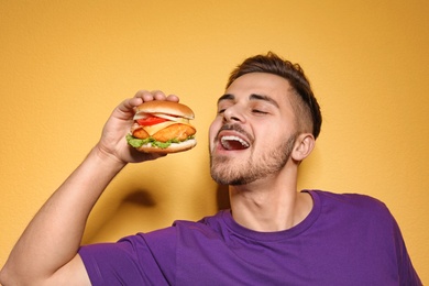 Photo of Handsome man eating tasty burger on color background