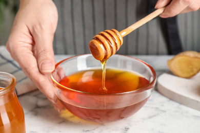 Photo of Woman with tasty honey at marble table, closeup