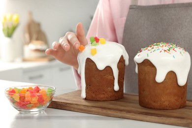 Photo of Woman decorating delicious Easter cake with pieces of candied fruits at white marble table in kitchen, closeup