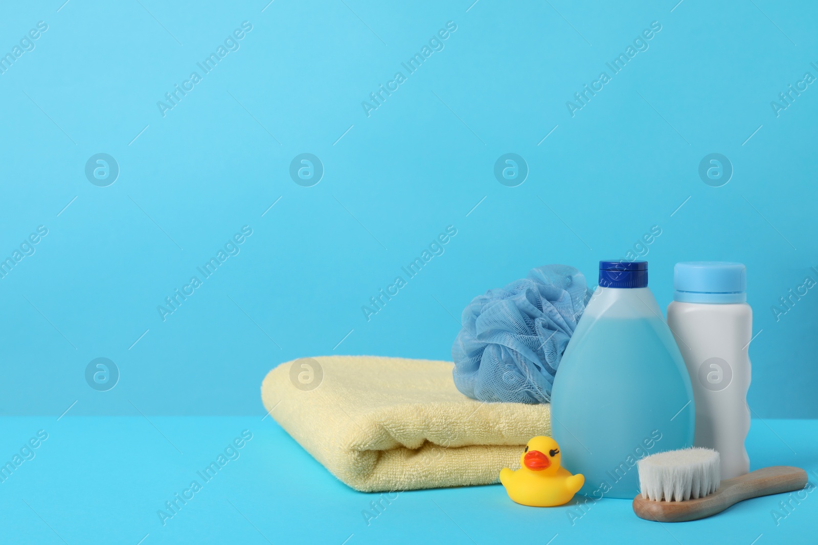 Photo of Baby cosmetic products, bath duck, accessories and towel on light blue background. Space for text
