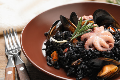 Photo of Delicious black risotto with seafood on wooden table, closeup