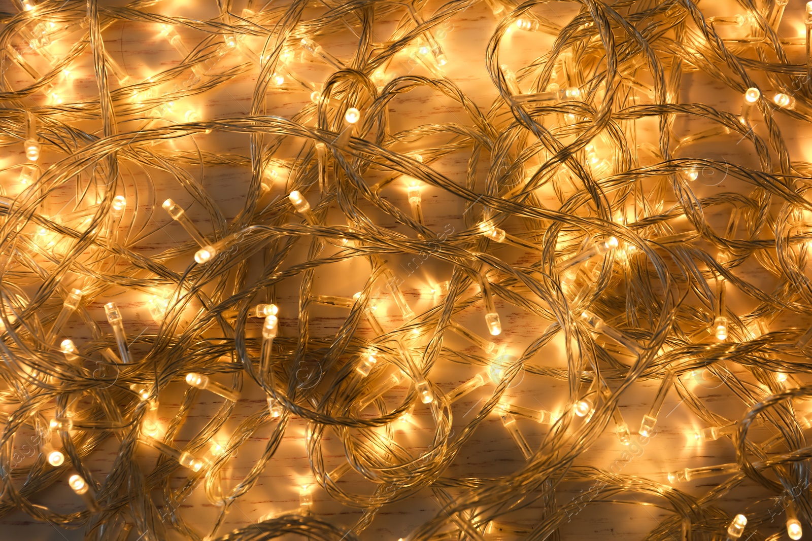 Photo of Glowing Christmas lights on white wooden background, top view