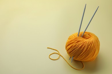 Photo of Soft woolen yarn and knitting needles on yellow background. Space for text
