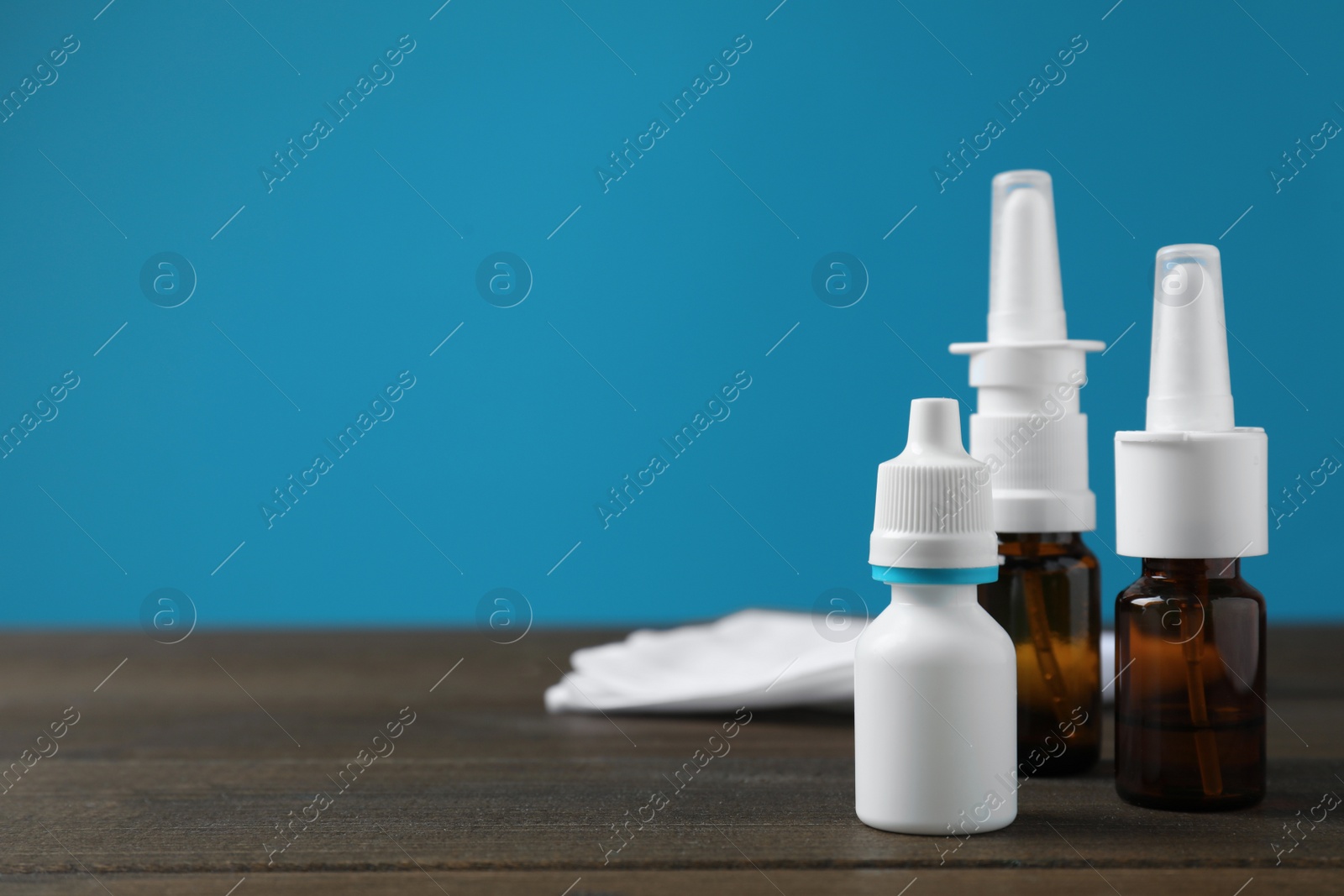 Photo of Nasal sprays in different bottles on wooden table against light blue background. Space for text