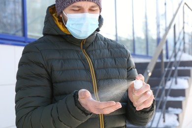 Man in protective mask spraying antiseptic onto hand outdoors