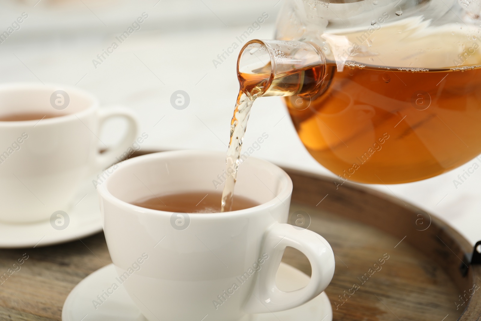 Photo of Pouring aromatic tea in cup at table, closeup