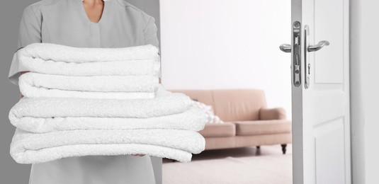 Image of Chambermaid with clean folded towels near door in hotel, closeup