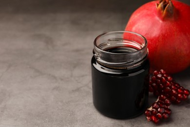 Photo of Glass jar of tasty pomegranate sauce and fresh ripe fruit on light grey table. Space for text