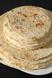 Many tasty homemade tortillas on black wooden table, closeup