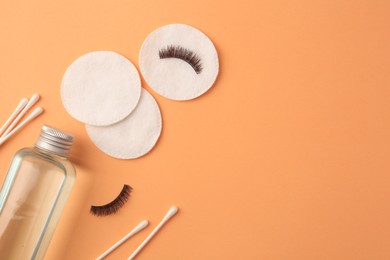 Flat lay composition with makeup remover and false eyelashes on pale orange background, space for text