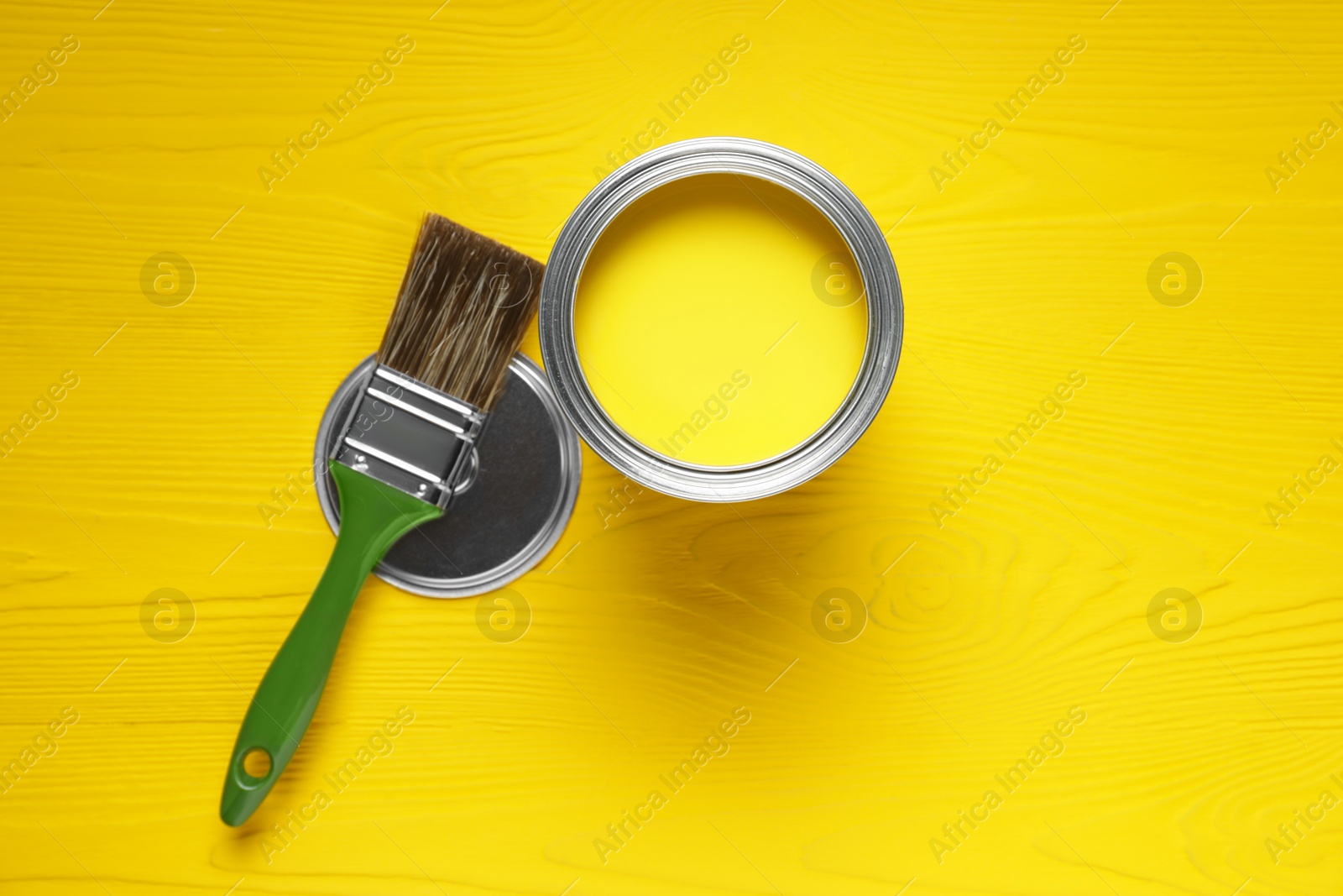 Photo of Can of yellow paint and brush on wooden table, flat lay