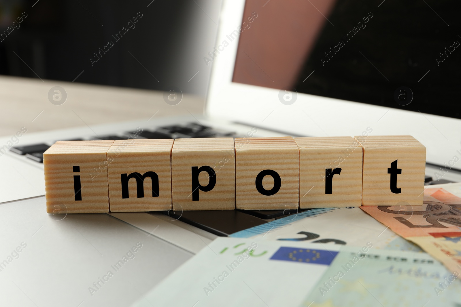 Photo of Word Import made of wooden cubes and banknotes on laptop, closeup