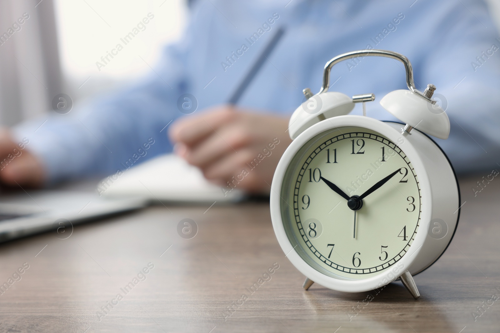 Photo of White alarm clock and man working at table, closeup. Space for text
