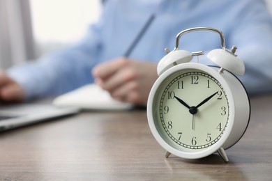 White alarm clock and man working at table, closeup. Space for text