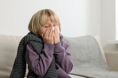 Photo of Boy blowing nose in tissue on sofa in room. Cold symptoms