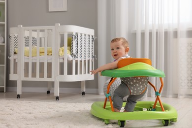 Photo of Cute baby making first steps with toy walker at home, space for text