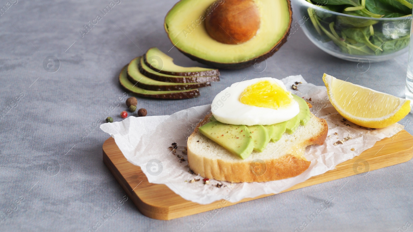 Photo of Delicious sandwich with boiled egg, pieces of avocado and lemon wedge on gray table