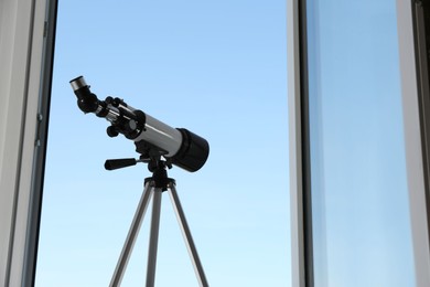 Photo of Tripod with modern telescope near open window indoors, low angle view. Space for text