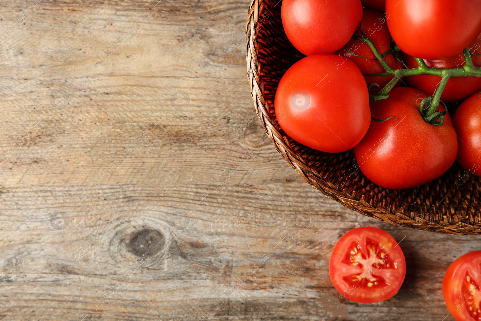 Photo of Fresh ripe red tomatoes in wicker bowl on wooden table, top view. Space for text