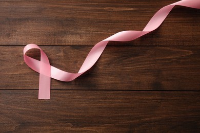 Photo of Pink ribbon on wooden table, top view with space for text. Breast cancer awareness concept