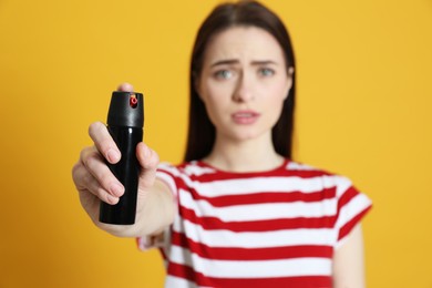 Young woman using pepper spray on yellow background
