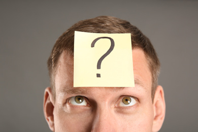 Photo of Emotional man with question mark on grey background, closeup