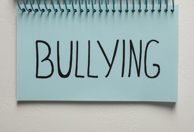 Photo of Word Bullying written in notebook on white stone surface, top view