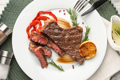 Photo of Delicious grilled beef steak with pepper, spices and lemon served on table, flat lay