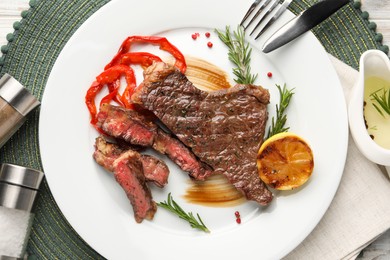 Delicious grilled beef steak with pepper, spices and lemon served on table, flat lay