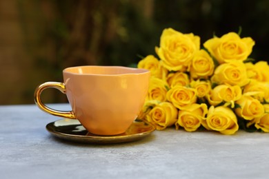 Cup of drink and beautiful yellow roses on light table outdoors, selective focus