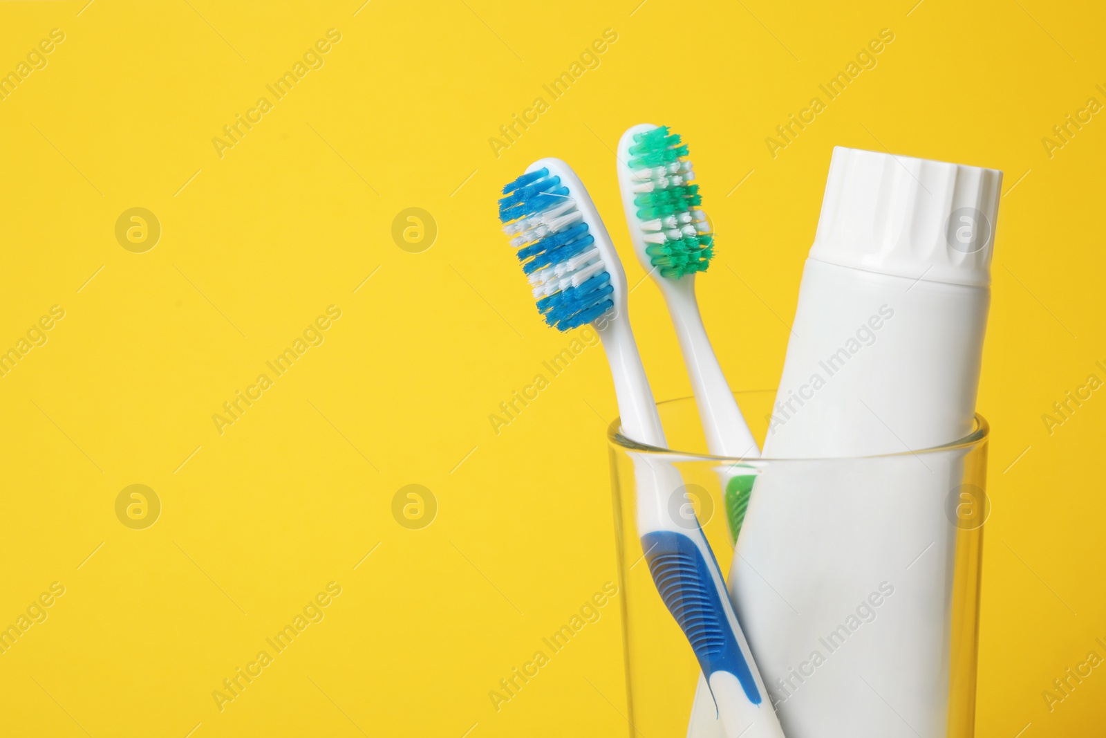 Photo of Glass with brushes and toothpaste on color background. Space for text