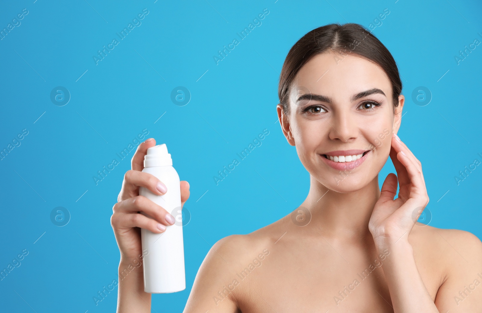 Photo of Young woman with bottle of thermal water on color background, space for text. Cosmetic product