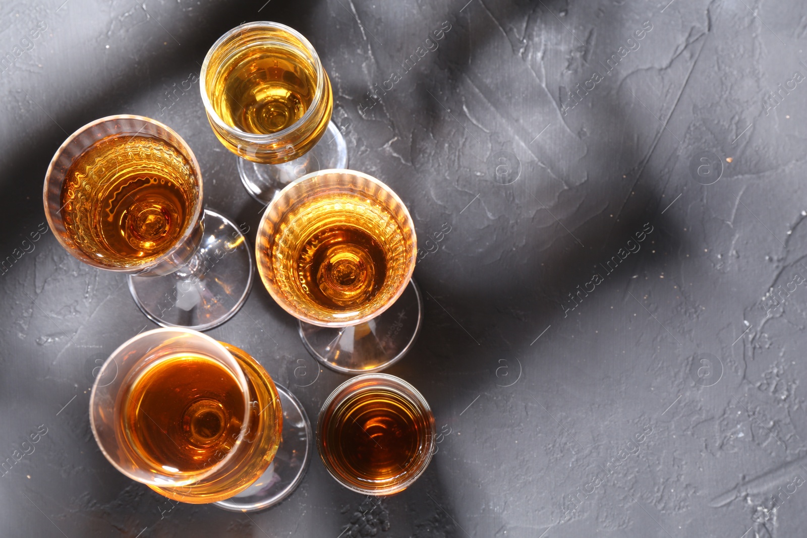 Photo of Many different liqueurs in glasses on dark textured table, flat lay. Space for text