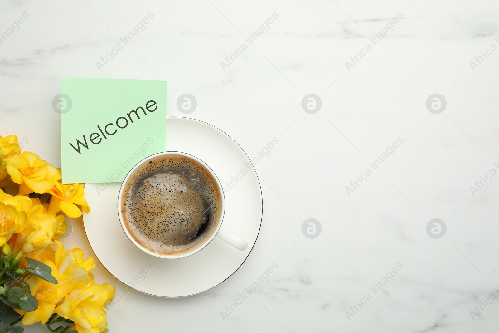 Image of Welcome card, beautiful yellow freesia flowers and cup of aromatic coffee on white marble table, flat lay