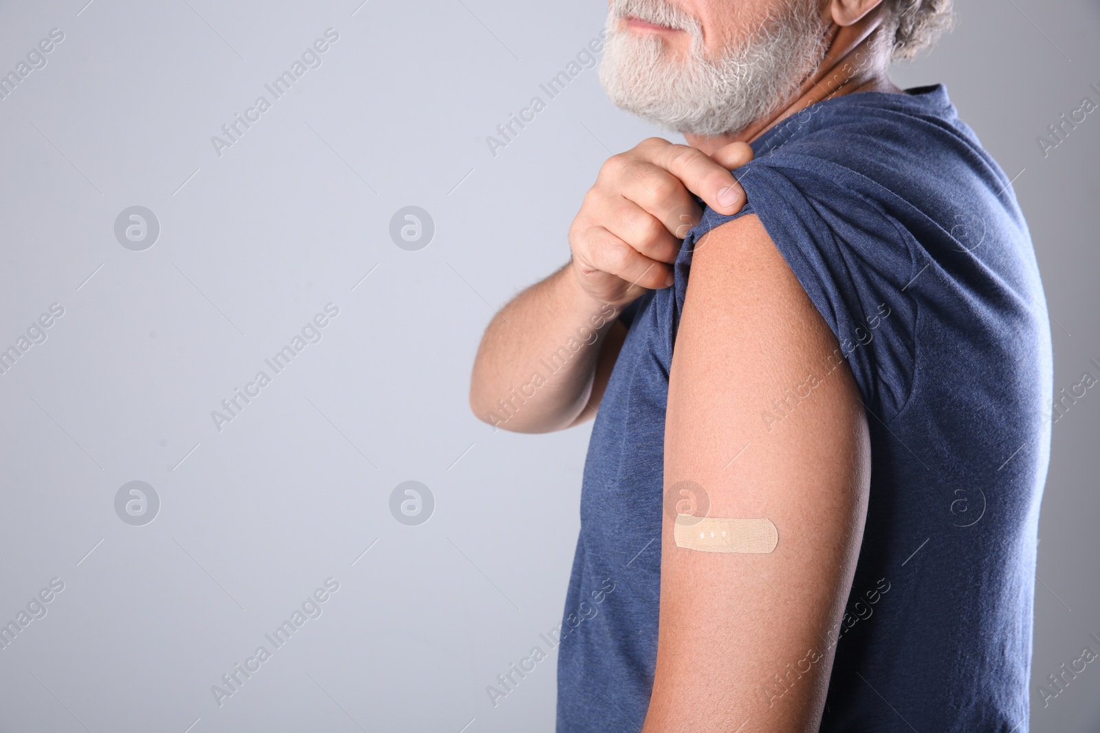 Photo of Senior man showing arm with bandage after vaccination on grey background, closeup. Space for text