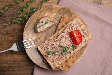 Photo of Crispy crackers with delicious meat pate and thyme served on wooden table, flat lay
