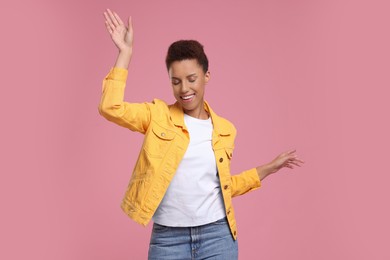 Happy young woman dancing on pink background