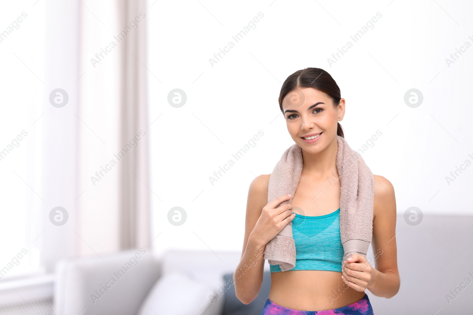 Photo of Beautiful young woman in sportswear with towel indoors. Space for text