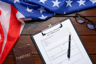 Photo of Visa application form for immigration, passport and American flag on wooden table, flat lay