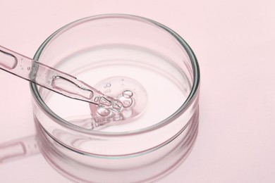 Glass pipette and petri dish with liquid on pink background, closeup