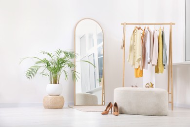 Stylish dressing room interior with mirror, ottoman and clothing rack